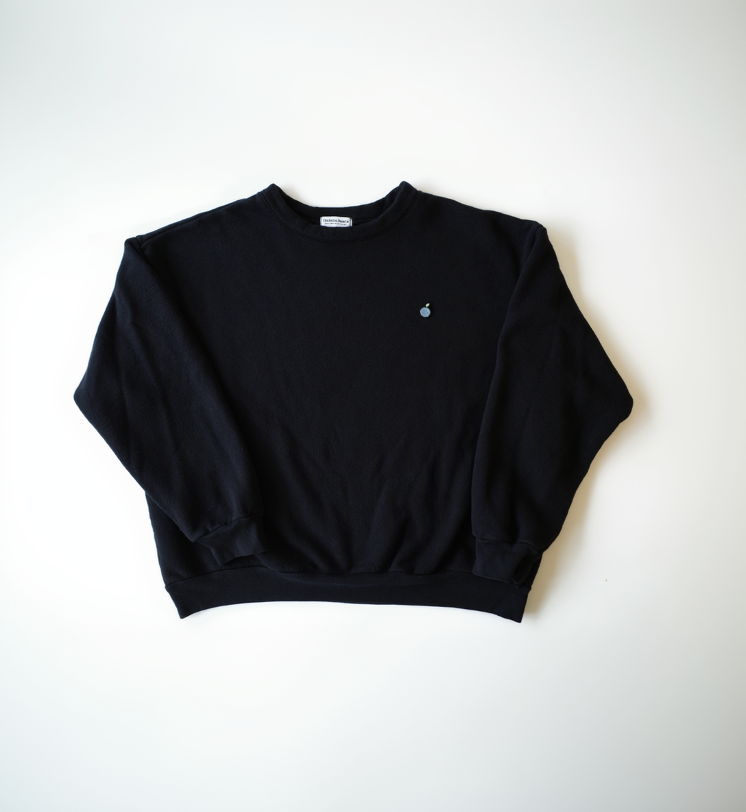 A washed black, crew neck, pullover sweatshirt laid flat on a white background.