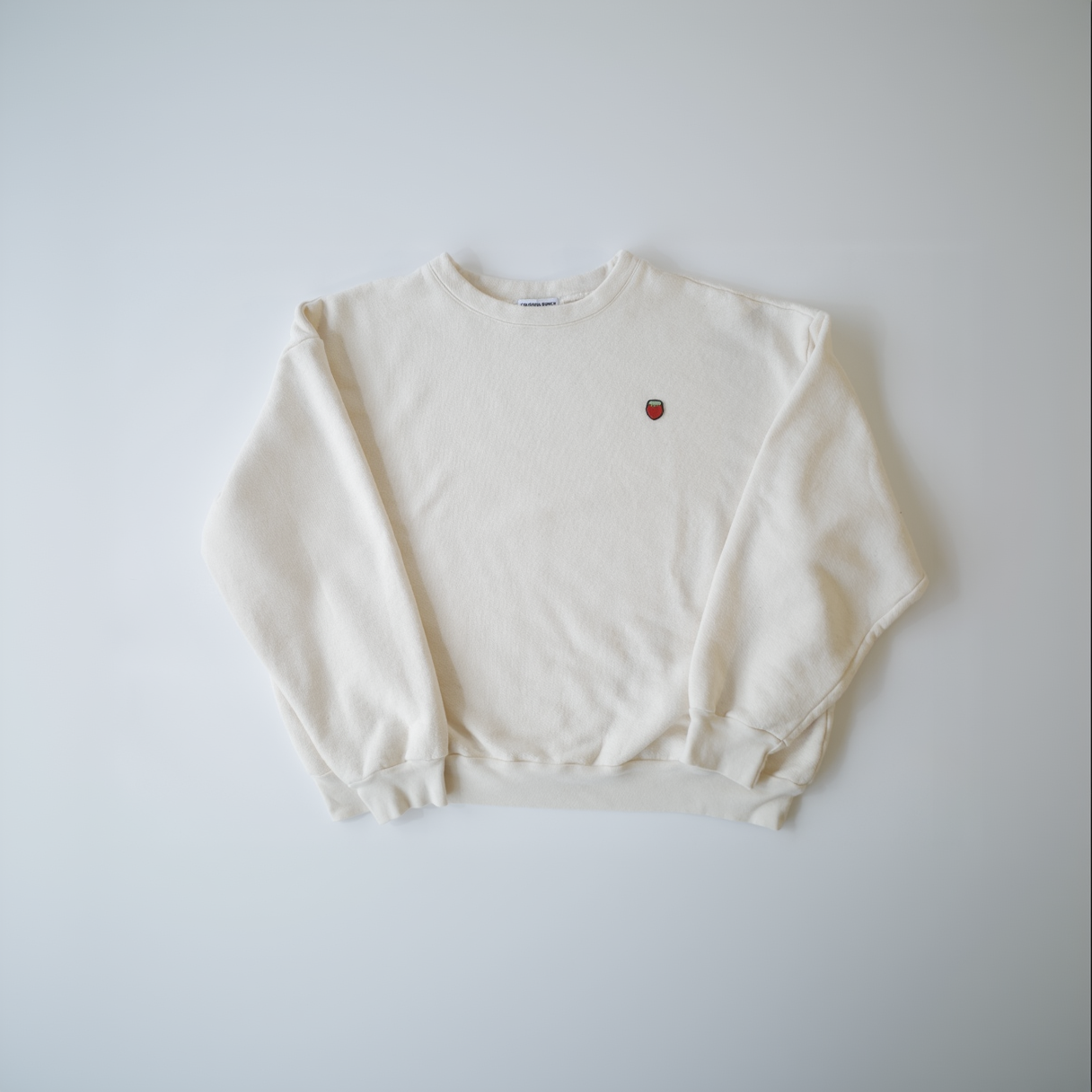 A unisex, crew neck sweatshirt in natural white color, made from organic cotton French Terry, with a small red logo on the chest.