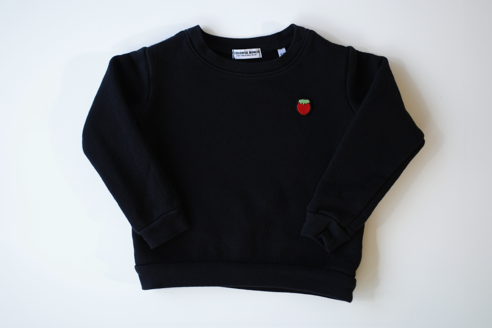 Classic black organic cotton children's sweatshirt, garment-dyed for exceptional softness with a retro look, featuring a vibrant embroidered strawberry, handcrafted in the USA by Colorful Bunch's environmentally conscious children's clothing line.