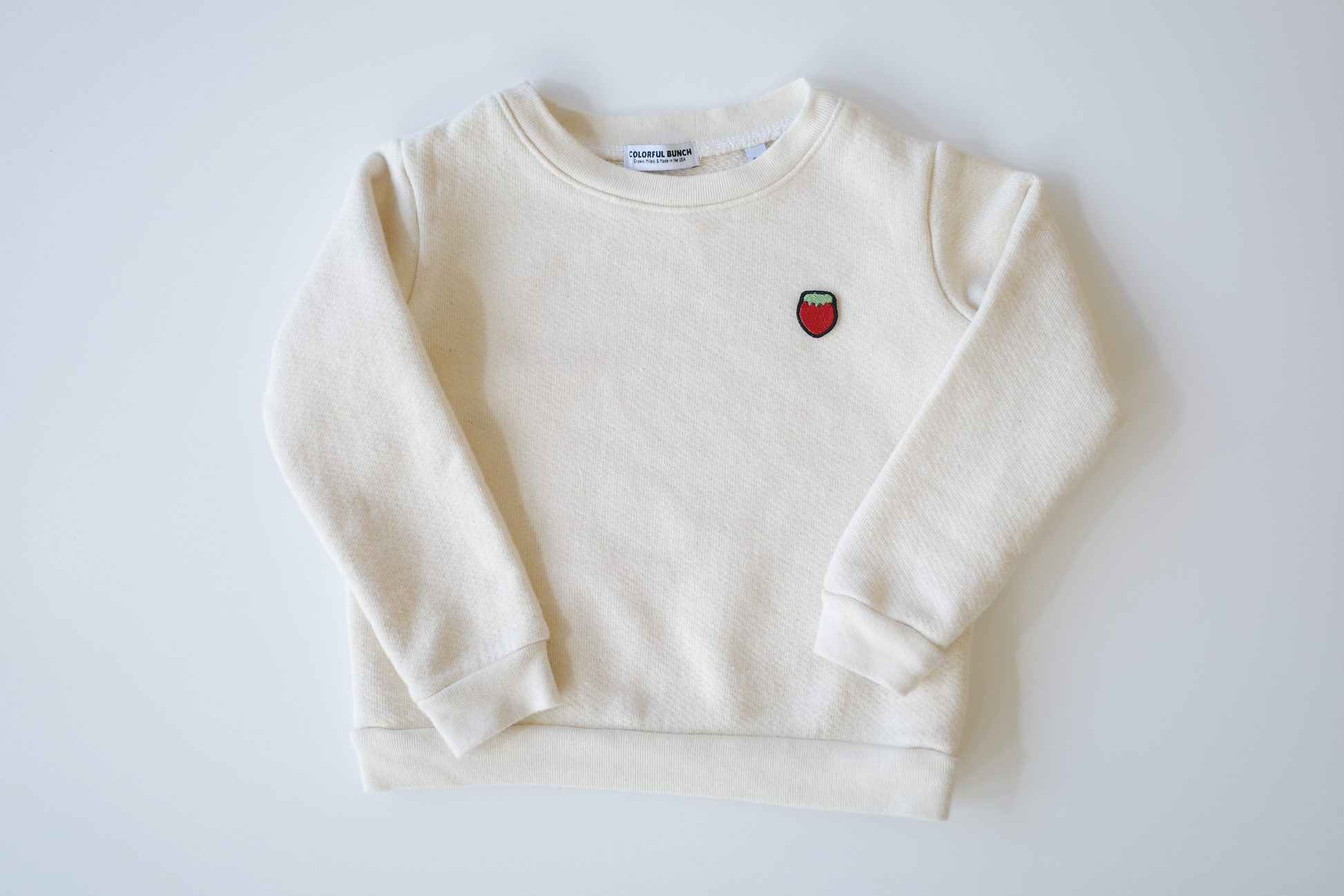 Unbleached, pure organic cotton children's sweater showcasing a sweet strawberry embroidery, sourced and crafted in the USA, part of Colorful Bunch's eco-friendly apparel collection for kids.