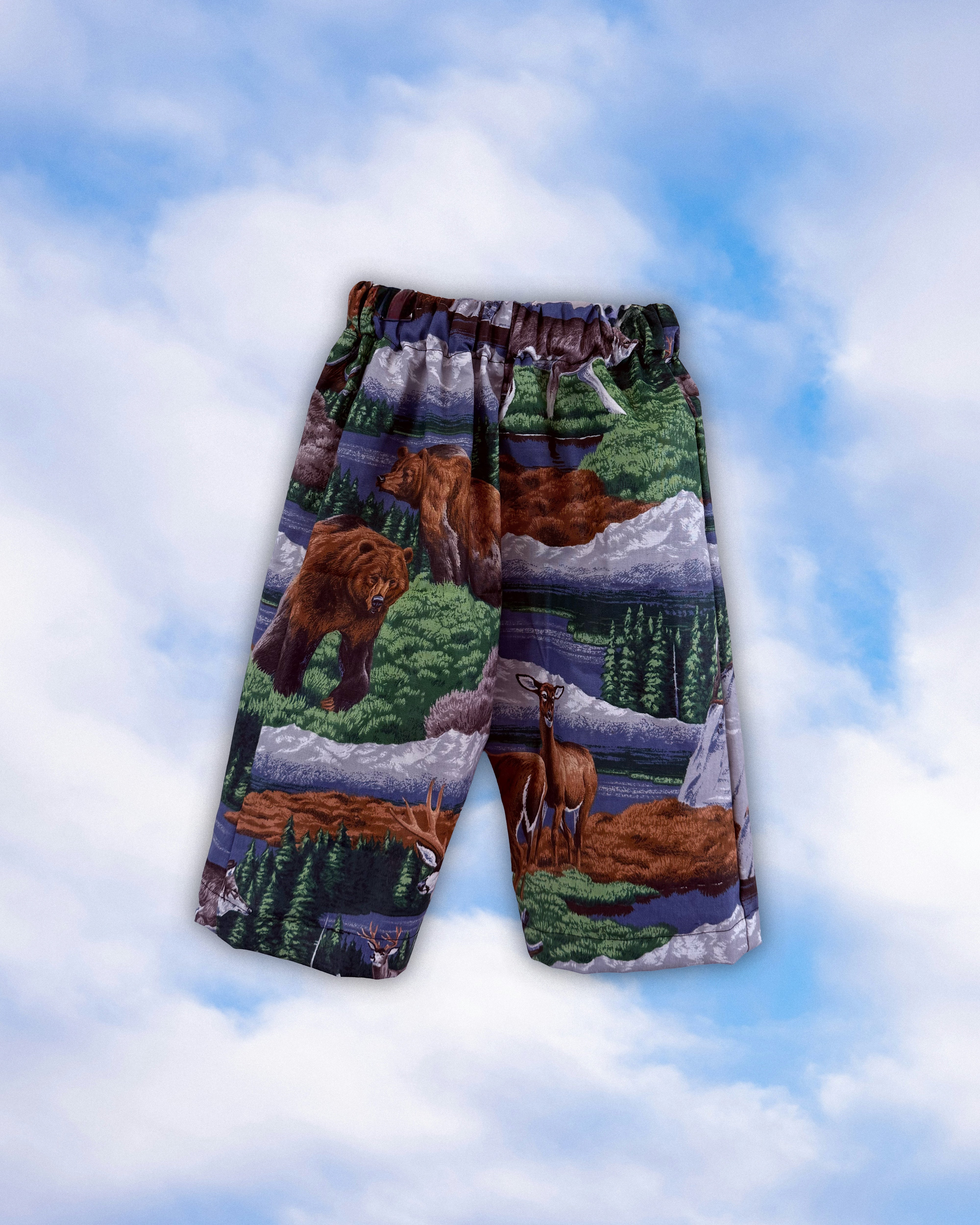 Sample children’s pull-on pants with a woodland bear and deer print on a blue sky background