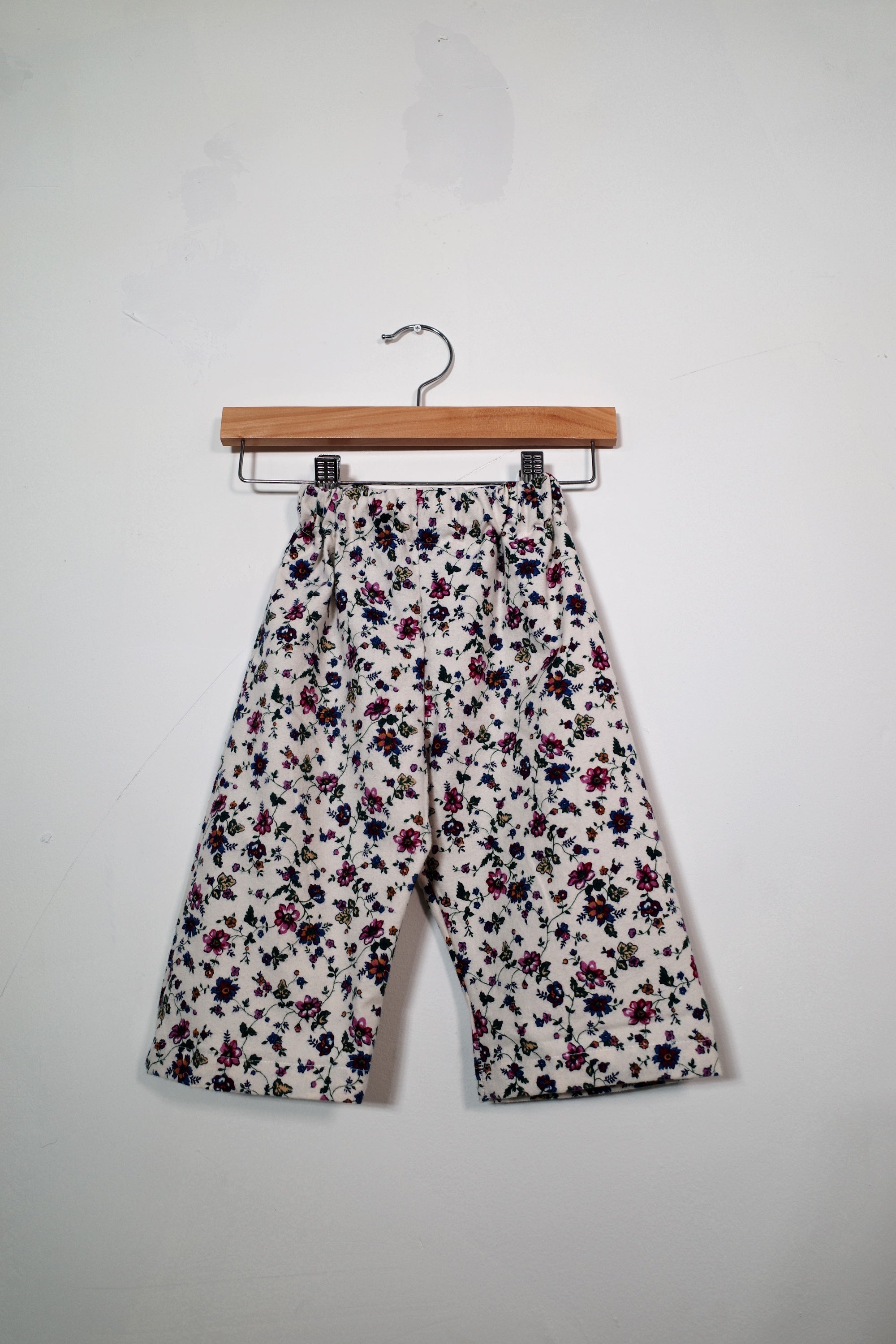 Kids’ pull-on pants in little wildflowers, shown hanging from a wooden hanger.