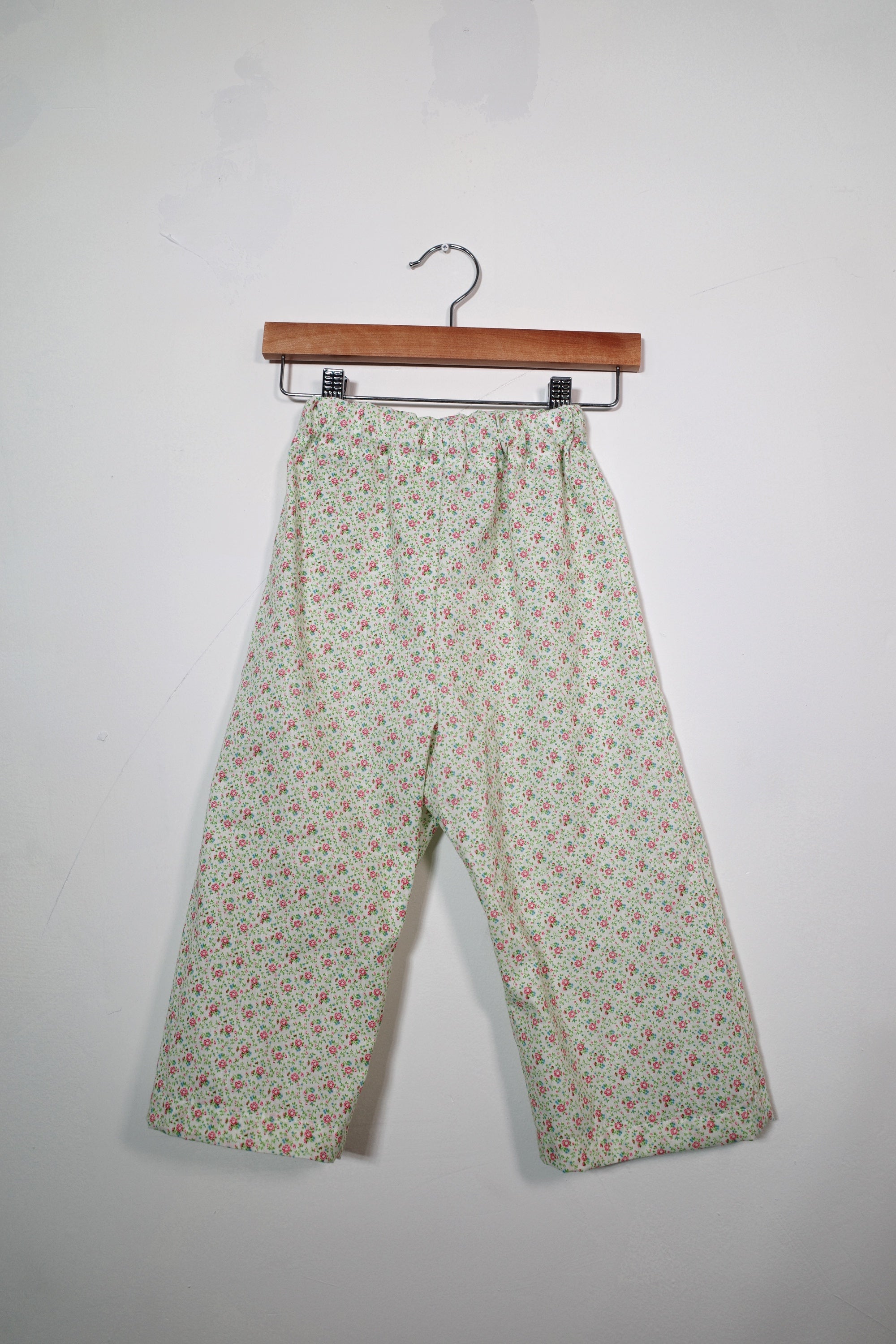 Kids’ pull-on pants in rosebud floral, shown hanging from a wooden hanger.